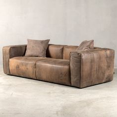 a brown leather couch sitting on top of a cement floor next to a white wall