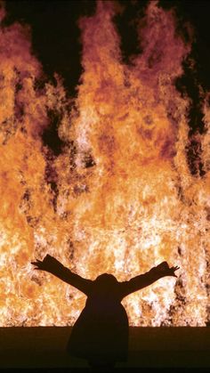 a person standing in front of a large fire with their arms spread out and hands outstretched