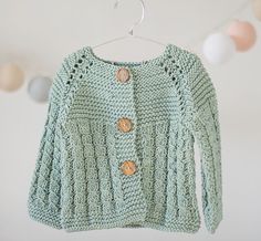 a green knitted sweater hanging from a clothes line with buttons on the front and back