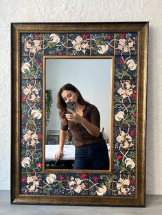 a woman looking at her cell phone in front of a mirror with flowers on it