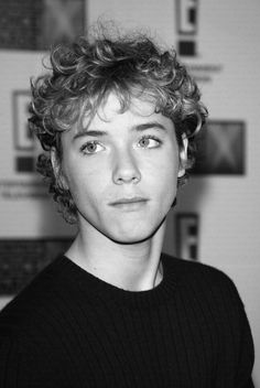 a black and white photo of a young man with curly hair looking at the camera