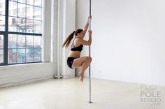 a woman is doing pole dancing in front of a window with her hands on the pole