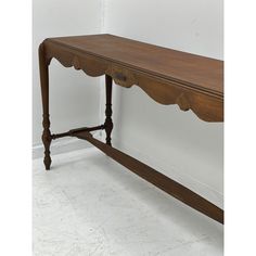 an old wooden table with scalloped edges on the top, against a white wall