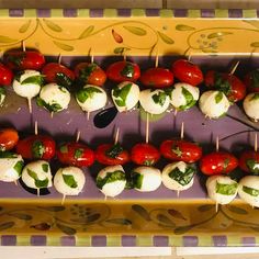 several skewered tomatoes and mozzarella are on a purple platter with spoons