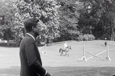 black and white photograph of two men on horses in an open field with trees behind them