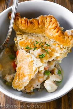 a bowl filled with chicken pot pie on top of a wooden table next to a fork