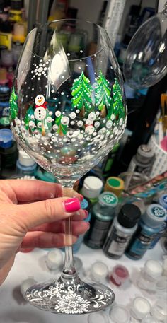 a hand holding a wine glass with snowmen painted on the side and trees in the middle