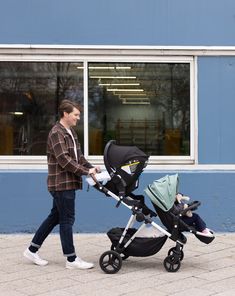 a man pushing a stroller with a baby in it down a sidewalk next to a building