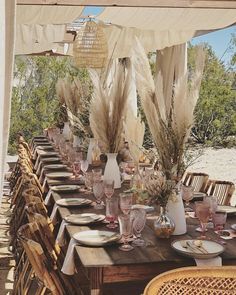 an outdoor dining table set with place settings and vases filled with pamodia