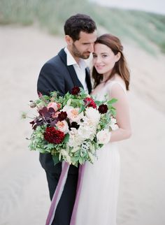 a bride and groom standing on the beach with their bouquets in front of them