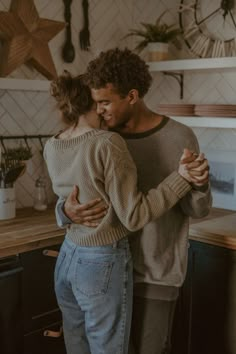 a man and woman hug in the kitchen while they stand next to each other with their arms around each other