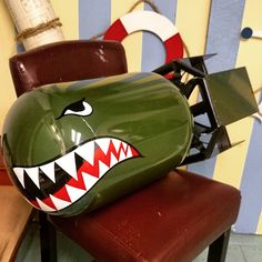 a green tank with a shark's mouth painted on it sitting on top of a red chair