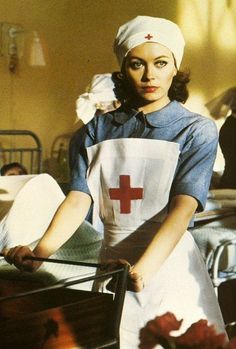 a woman with a red cross on her shirt and white apron is standing next to a bed