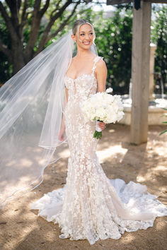 a woman in a wedding dress and veil holding a bouquet standing under a gazebo