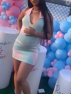 a pregnant woman standing in front of balloons with her hands on her hips, wearing a pink and blue dress