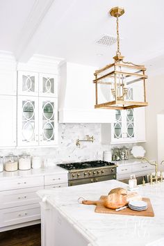 a kitchen with white cabinets and marble counter tops, an island in front of the stove