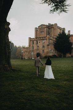 a bride and groom holding hands in front of an old castle