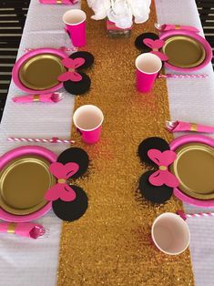 a table set up for a minnie mouse party with pink and black plates, cups, napkins and flowers