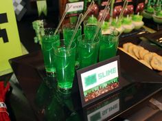 some green drinks are sitting on a table with other foods and desserts in the background