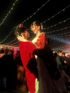 a man and woman dancing in front of a crowd at a party with string lights on the ceiling