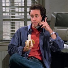 a man sitting down while talking on a cell phone and holding a banana in his hand