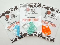 three bags of popcorn time necklaces on top of a cow print tablecloth with tags attached to them