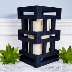 a candle holder made out of wooden blocks with green leaves around it on a marble countertop