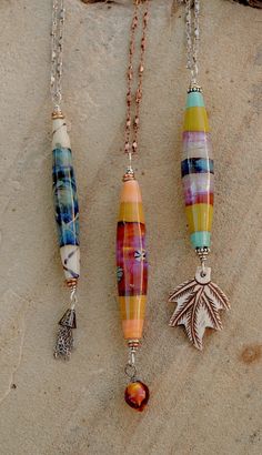 three necklaces with different designs on them sitting next to each other in the sand