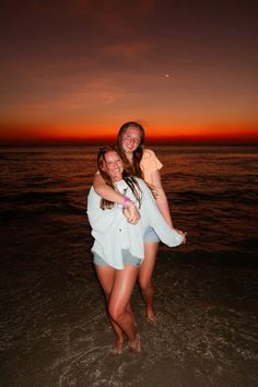 two women are hugging on the beach at sunset