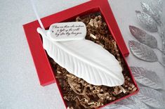 a white feather ornament in a red box