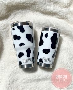 two black and white cow print tumblers sitting on top of a blanket