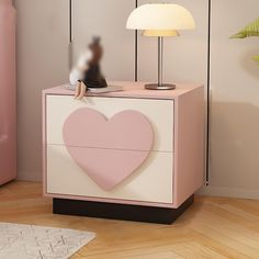 a pink and white nightstand with a heart cut out on the top, next to a lamp