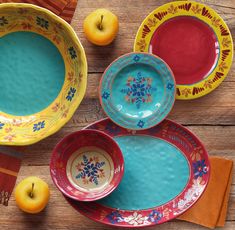 four colorful plates and two oranges on top of a wooden table with napkins