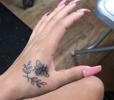 a woman's hand with a flower tattoo on her left wrist and pink nail polish