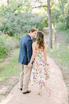 a man and woman standing next to each other on a path in front of trees