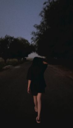 a woman walking down the road at night with her back turned to the camera,