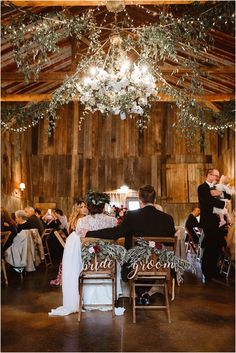 a bride and groom are sitting at the table in front of their guests, with chandelier hanging from the ceiling