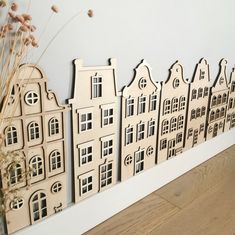 there is a wooden cutout of houses on the wall next to a vase with dried flowers in it