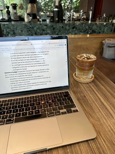 an open laptop computer sitting on top of a wooden table next to a cup of coffee