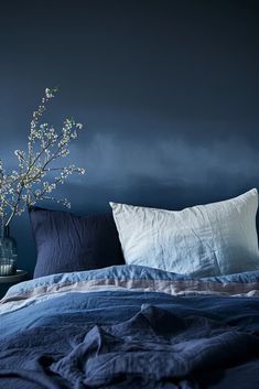 a bed with blue sheets, pillows and a vase filled with flowers on top of it