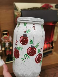 someone holding up a painted mason jar with christmas ornaments on it