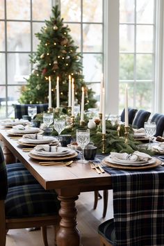 a dining room table set for christmas dinner with candles and plaid napkins on it