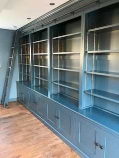 an empty room with blue bookcases and ladder in the center, on hard wood flooring