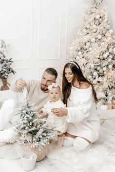 a man and woman sitting next to a baby in front of a christmas tree