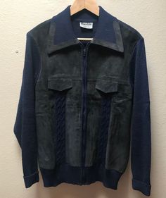 a black jacket hanging on a wall next to a hanger with a blue sweater