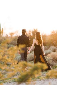 a man and woman holding hands while walking through the desert with cactus in the background