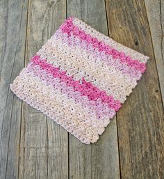 a pink and white crocheted blanket laying on top of a wooden floor