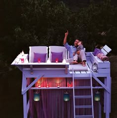 a man and woman sitting on top of a tree house with candles in the trees