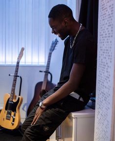 a man sitting on top of a white counter next to two guitar's in a room