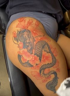 a woman's thigh with an elephant and flowers tattoo on her leg, sitting in a chair